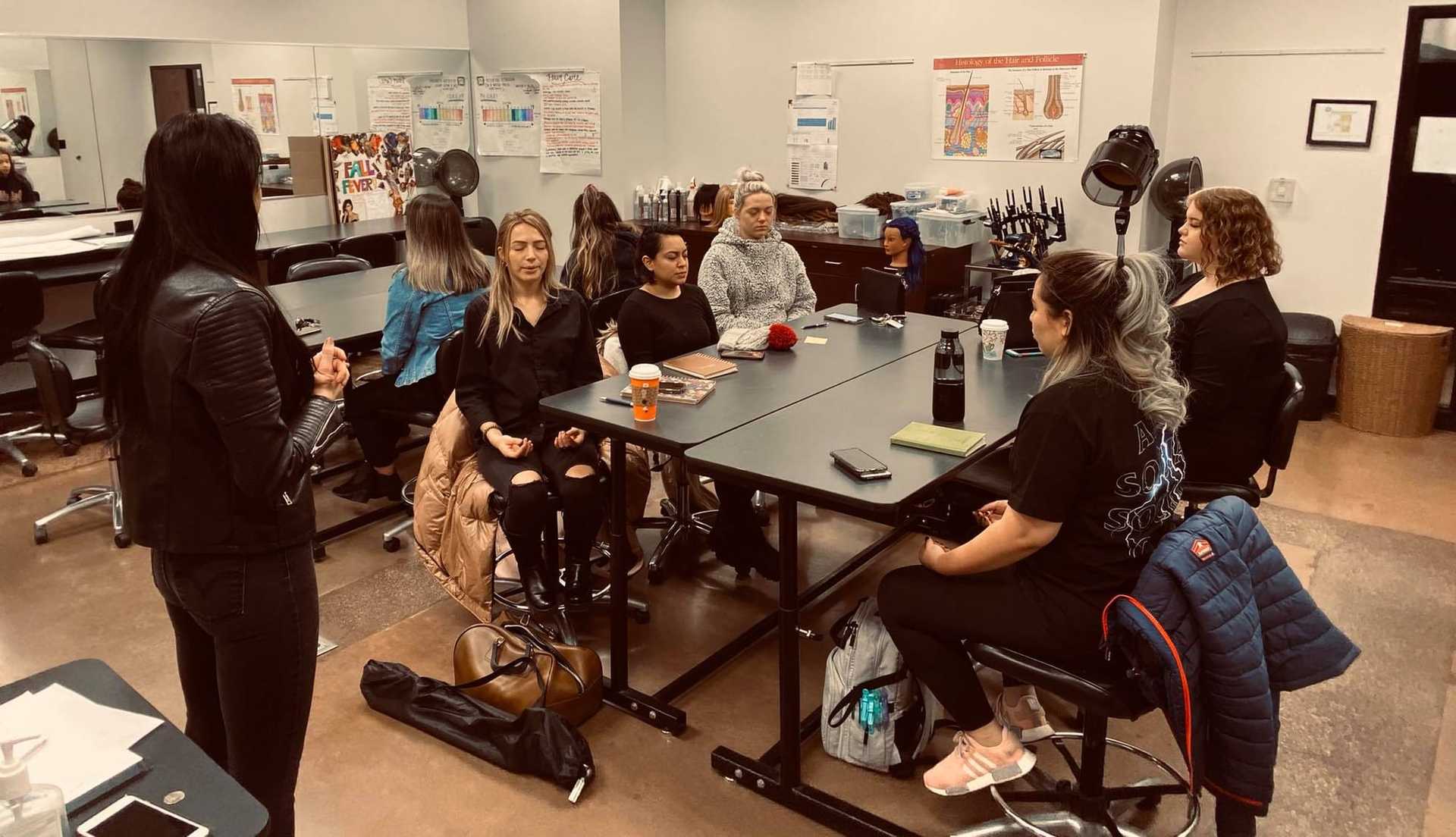 Group of people having a meeting in a classroom with posters and hairdressing tools.